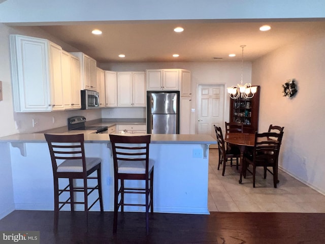 kitchen featuring a peninsula, hanging light fixtures, stainless steel appliances, a kitchen bar, and white cabinetry