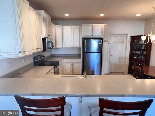 kitchen with decorative light fixtures, stainless steel appliances, white cabinetry, a peninsula, and a kitchen bar