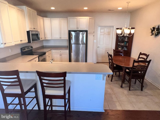 kitchen featuring a peninsula, white cabinetry, a kitchen bar, and appliances with stainless steel finishes