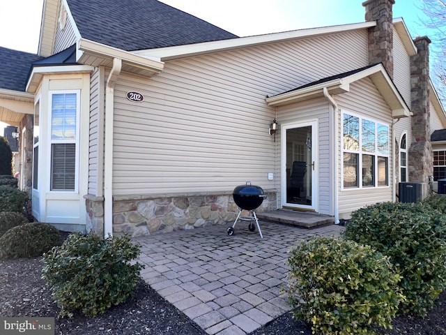 entrance to property featuring stone siding, a shingled roof, a chimney, and a patio area