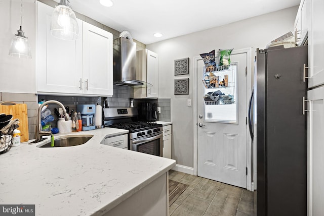 kitchen featuring a sink, white cabinetry, wall chimney range hood, freestanding refrigerator, and stainless steel range with gas stovetop