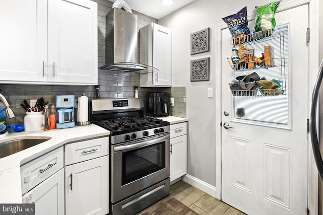 kitchen featuring tasteful backsplash, white cabinetry, wall chimney range hood, and stainless steel gas range oven