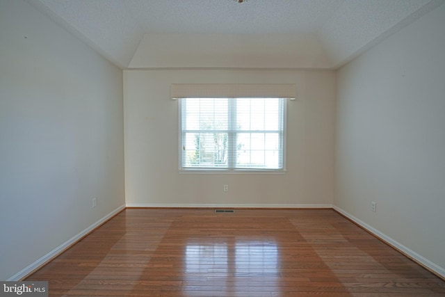 empty room featuring wood-type flooring, visible vents, a textured ceiling, and baseboards