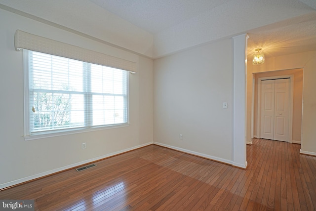 empty room with hardwood / wood-style flooring, baseboards, visible vents, and a notable chandelier