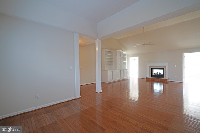 unfurnished living room featuring baseboards, a fireplace with raised hearth, ceiling fan, wood finished floors, and vaulted ceiling