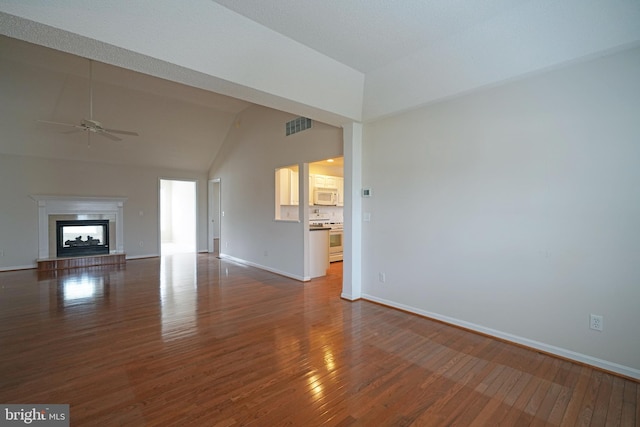 unfurnished living room featuring ceiling fan, visible vents, a fireplace with raised hearth, and wood finished floors