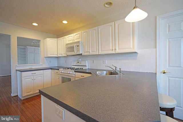 kitchen with white appliances, dark countertops, a sink, and white cabinets