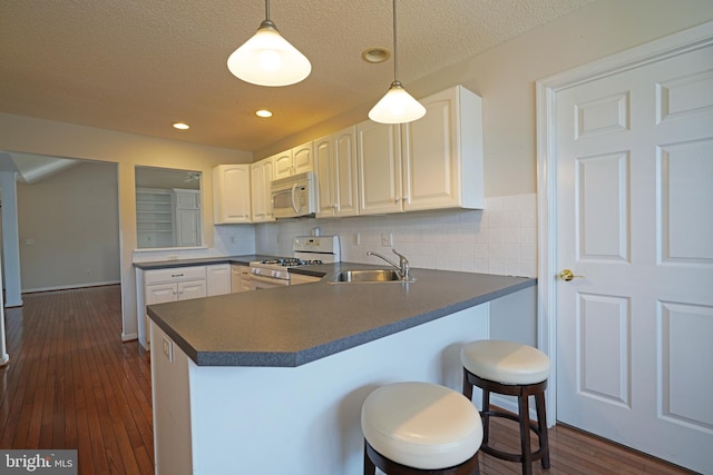 kitchen featuring dark countertops, a sink, white appliances, a peninsula, and a kitchen breakfast bar