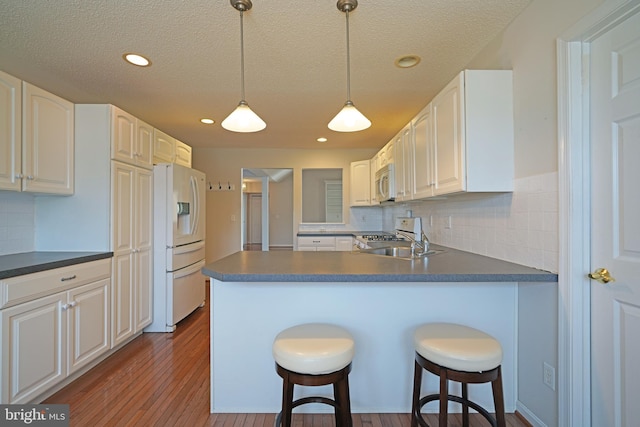 kitchen featuring a peninsula, white appliances, dark countertops, and a breakfast bar