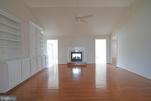 unfurnished living room with a fireplace with raised hearth, ceiling fan, vaulted ceiling, wood finished floors, and baseboards