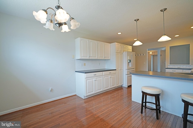 kitchen featuring white refrigerator with ice dispenser, dark countertops, light wood-style flooring, a kitchen breakfast bar, and white cabinetry