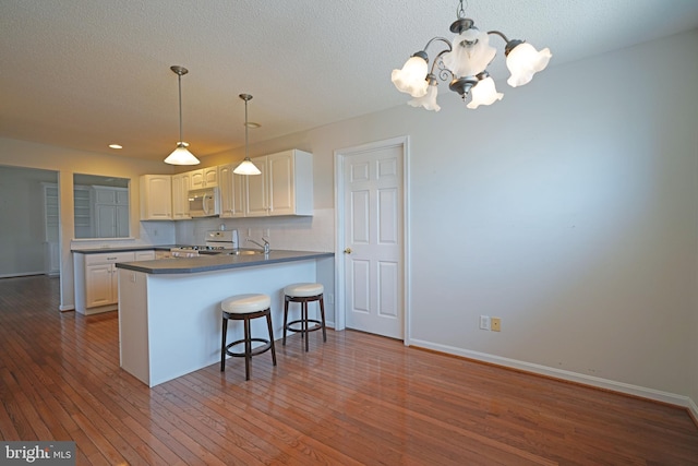 kitchen with dark countertops, backsplash, white appliances, a peninsula, and hardwood / wood-style flooring