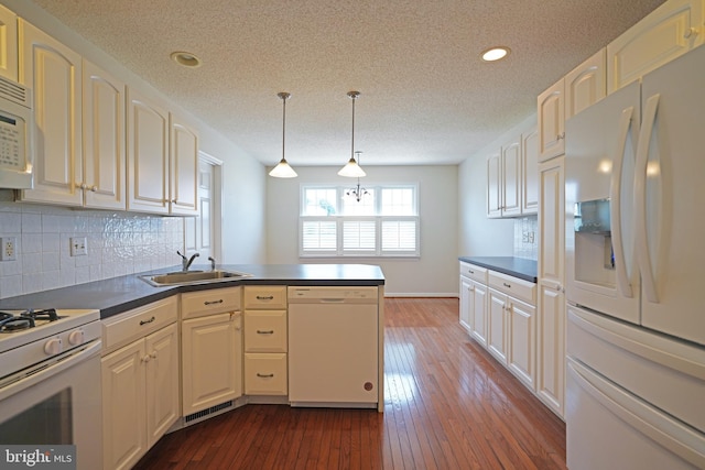 kitchen with dark wood-style flooring, dark countertops, a sink, white appliances, and a peninsula