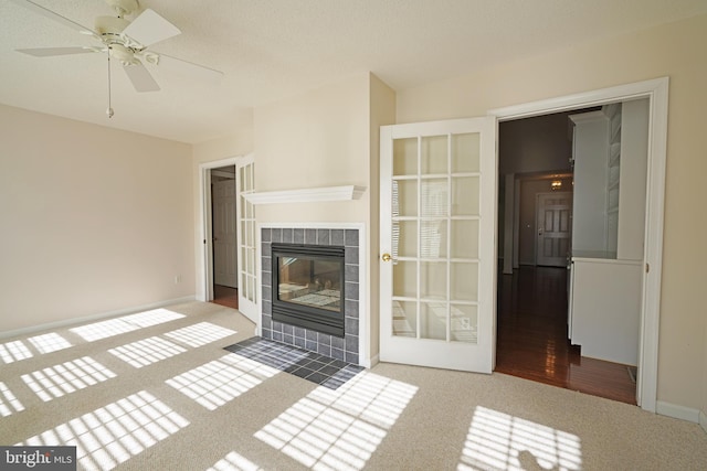 unfurnished living room featuring a tile fireplace, carpet flooring, ceiling fan, and baseboards