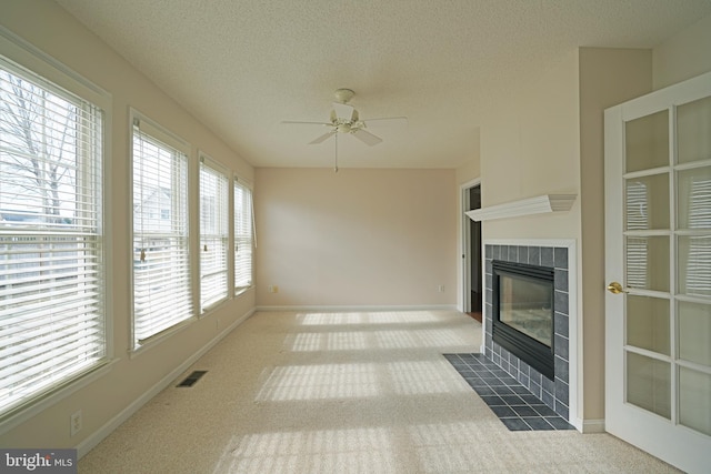 unfurnished living room with carpet, visible vents, a textured ceiling, and a tile fireplace