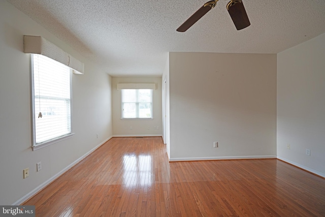 empty room featuring light wood finished floors, baseboards, and a textured ceiling