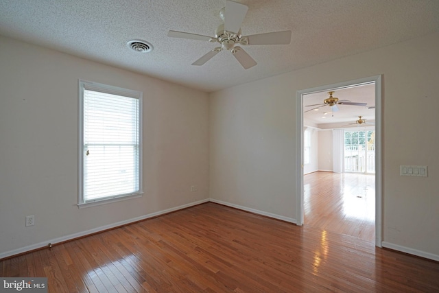 unfurnished room with a textured ceiling, visible vents, hardwood / wood-style flooring, and baseboards