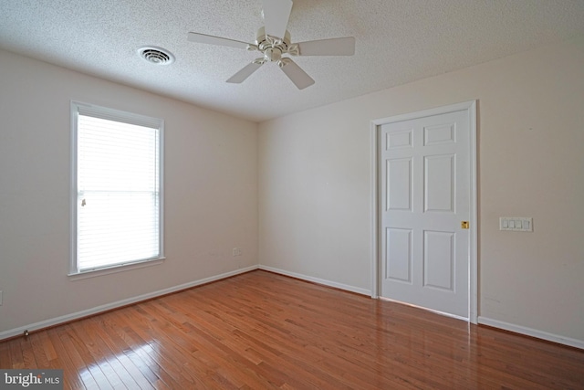 unfurnished bedroom with a textured ceiling, ceiling fan, visible vents, baseboards, and hardwood / wood-style floors