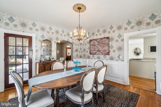 dining space featuring arched walkways, wainscoting, wallpapered walls, hardwood / wood-style floors, and an inviting chandelier