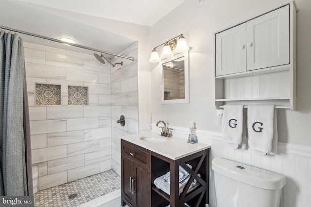 bathroom with vanity, wainscoting, a tile shower, and toilet