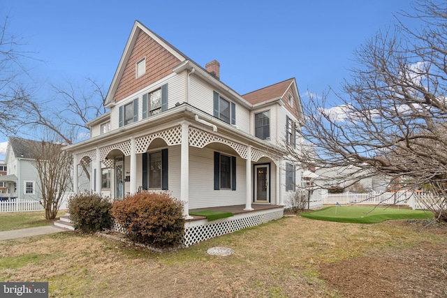 view of front of house with covered porch, fence, a chimney, and a front lawn