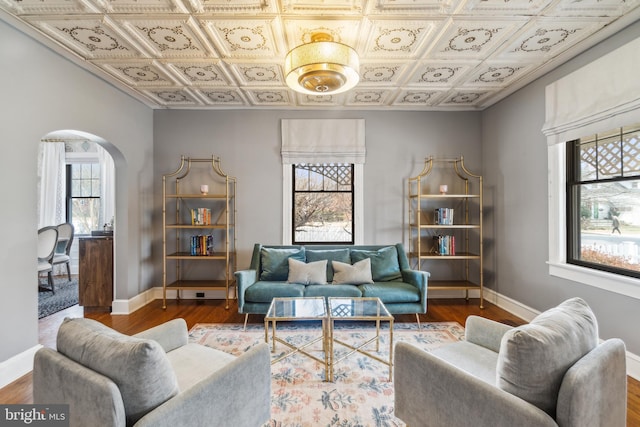 living area with arched walkways, wood finished floors, an ornate ceiling, and baseboards