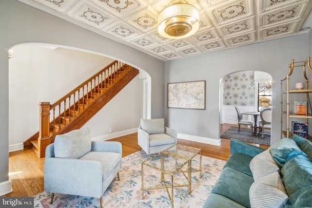 living area featuring arched walkways, wood finished floors, baseboards, stairs, and an ornate ceiling