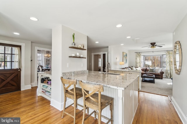 kitchen featuring a peninsula, a sink, light wood-style floors, light stone countertops, and open shelves