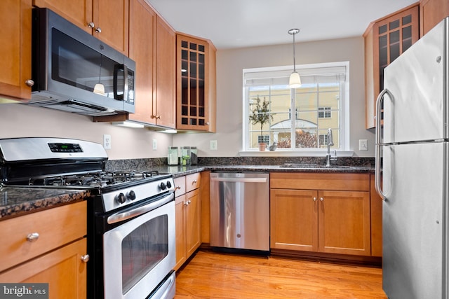 kitchen with light wood-type flooring, glass insert cabinets, stainless steel appliances, and a sink