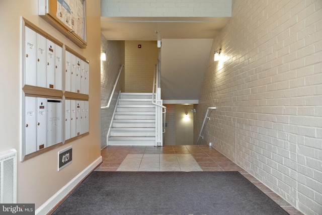 staircase featuring brick wall, tile patterned flooring, mail area, and visible vents