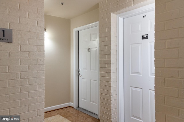 interior space featuring baseboards, light tile patterned flooring, and brick wall