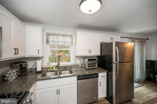 kitchen featuring dark stone counters, appliances with stainless steel finishes, white cabinetry, a sink, and dark wood-style floors