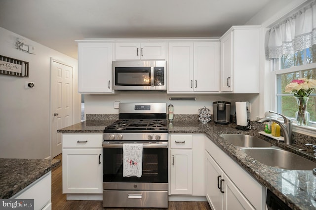 kitchen with dark wood-style flooring, dark stone counters, appliances with stainless steel finishes, white cabinetry, and a sink