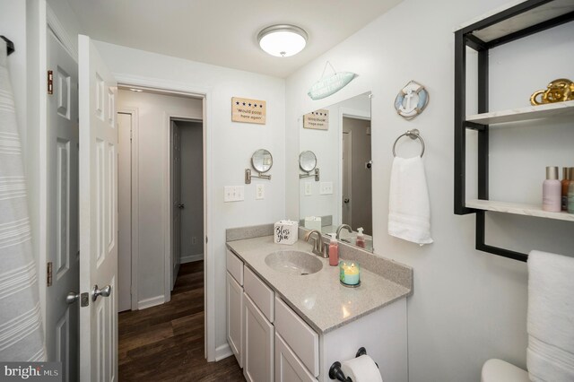 bathroom featuring baseboards, wood finished floors, toilet, and vanity
