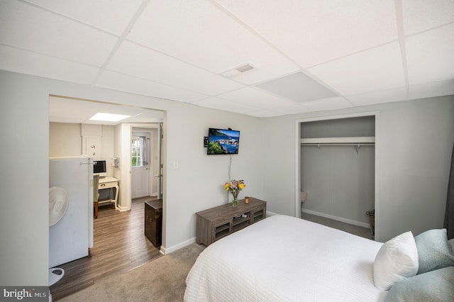 bedroom featuring a closet, visible vents, baseboards, wood finished floors, and a paneled ceiling