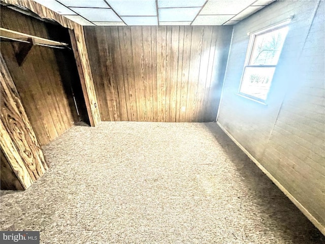 empty room with a drop ceiling, wood walls, and carpet