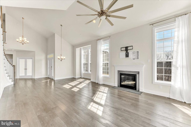 unfurnished living room with stairs, a chandelier, wood finished floors, and a glass covered fireplace