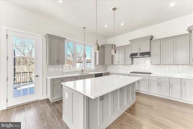 kitchen featuring light countertops, a sink, decorative light fixtures, and under cabinet range hood