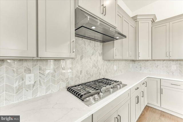 kitchen with light stone counters, tasteful backsplash, stainless steel gas stovetop, light wood-style floors, and under cabinet range hood