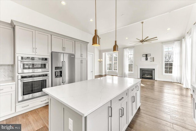 kitchen featuring a fireplace, a kitchen island, open floor plan, appliances with stainless steel finishes, and light stone countertops