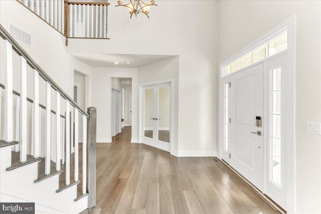 foyer with light wood finished floors, stairway, a towering ceiling, and visible vents