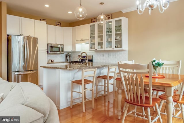 kitchen featuring decorative backsplash, glass insert cabinets, light stone countertops, stainless steel appliances, and white cabinetry