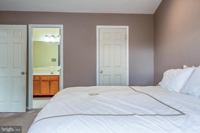 bedroom featuring light colored carpet, a sink, and ensuite bath