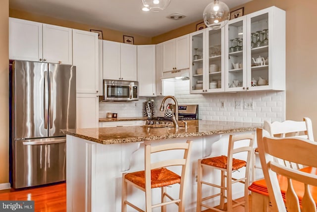 kitchen featuring stainless steel appliances, a peninsula, white cabinets, and light stone countertops