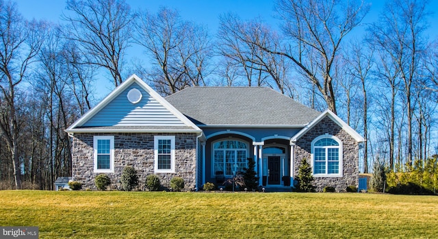 view of front facade with a front yard, stone siding, and roof with shingles