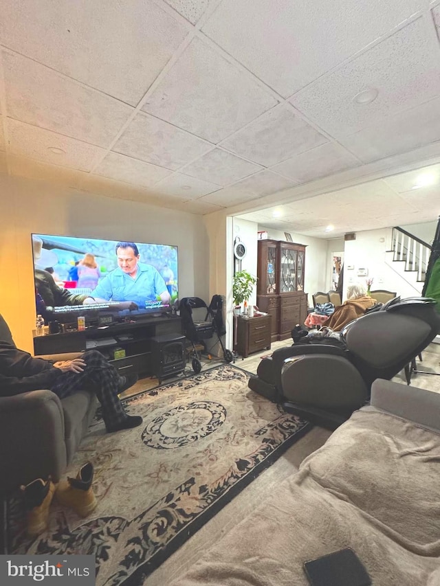 living area with stairs, carpet floors, and a drop ceiling