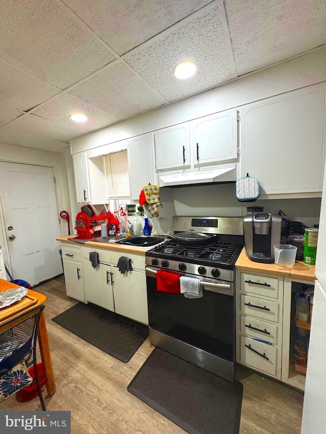 kitchen with under cabinet range hood, white cabinets, light wood-style floors, light countertops, and stainless steel range with gas stovetop