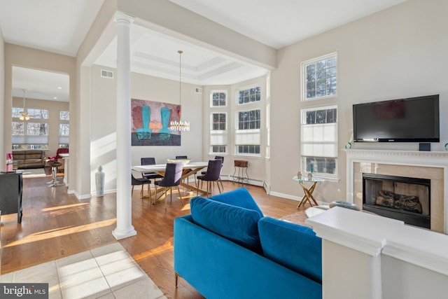 living room with a high end fireplace, visible vents, decorative columns, and wood finished floors