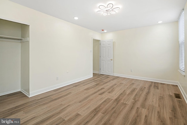 unfurnished bedroom with a closet, wood finished floors, visible vents, and baseboards