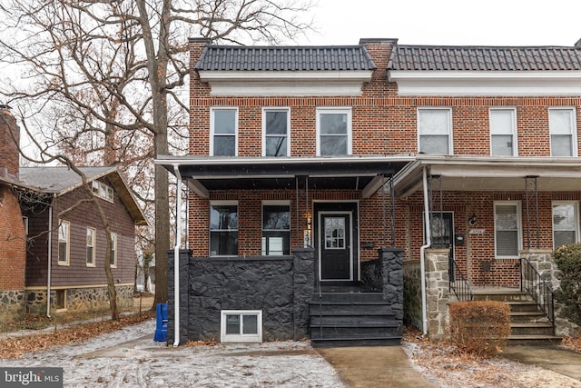 view of property featuring a porch, a tile roof, and brick siding